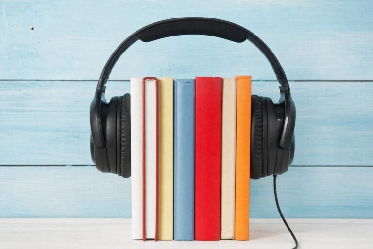 A pair of black over-ear headphones wrapped around a row of colorful books standing upright against a light blue wooden wall, soft daylight