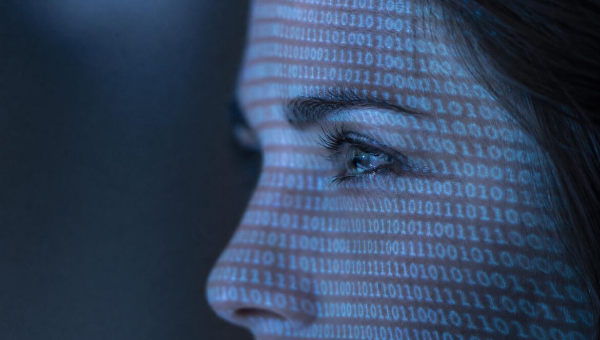 A persons face in profile with rows of blue binary numbers 0 and 1 projected across the skin pale blue light close up