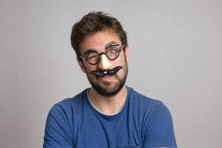 A playful portrait of a man wearing novelty glasses with a fake mustache, plain studio background