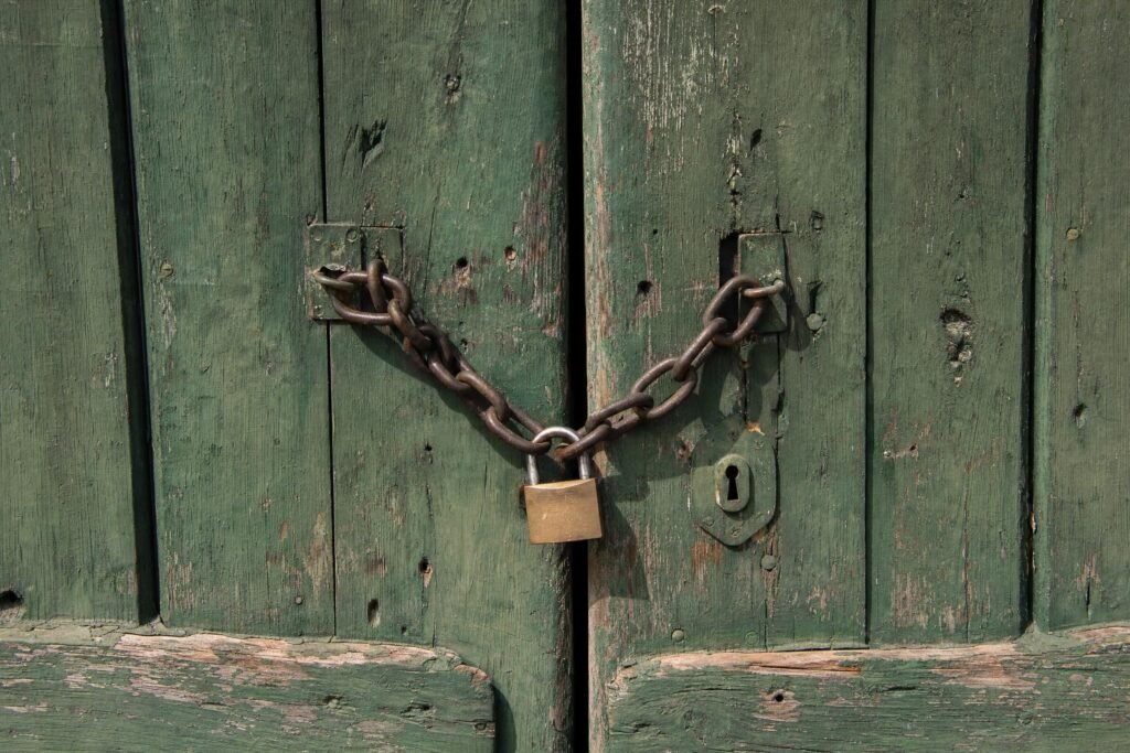 A rustic green wooden door secured with a heavy chain and padlock weathered paint daylight