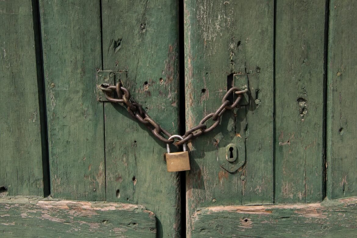 A rustic green wooden door secured with a heavy chain and padlock, weathered paint, daylight