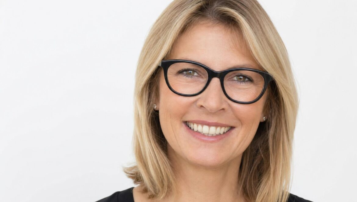 A smiling middleaged woman with shoulderlength blonde hair and thick blackrimmed glasses closeup head portrait against a plain white background in soft lig | edCircuit A smiling middle aged woman with shoulder length blonde hair and thick black rimmed glasses close up head portrait against a plain white background in soft lig
