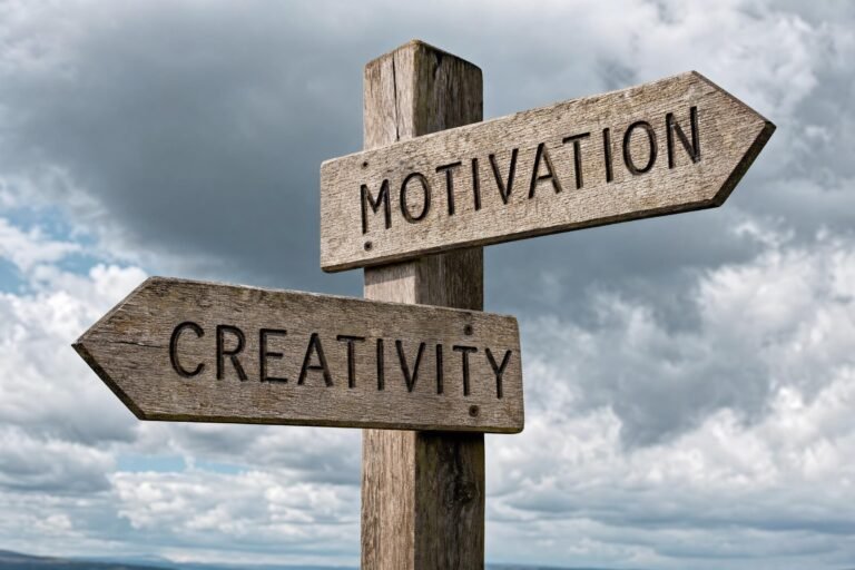 A weathered wooden signpost against a dramatic cloudy sky with two arrows reading MOTIVATION and CREATIVITY pointing in different directions