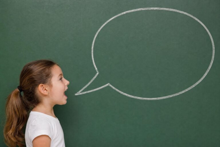 A young girl in profile with her mouth open as if speaking toward a large empty speech bubble drawn in white chalk on a green chalkboard