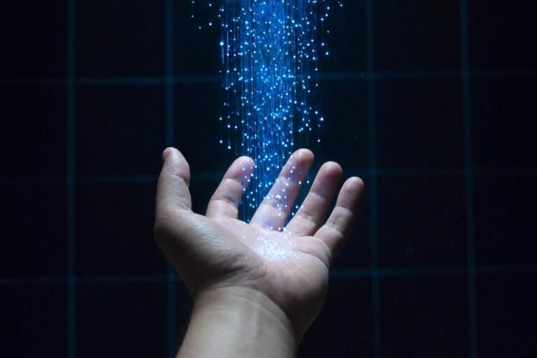 An open palm held up under a stream of tiny glowing blue lights falling from above, dark blue background with faint grid lines, cool lighting