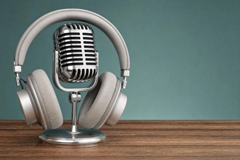 Silver headphones draped over a chrome vintage microphone on a wooden desk, plain teal wall behind, soft studio light