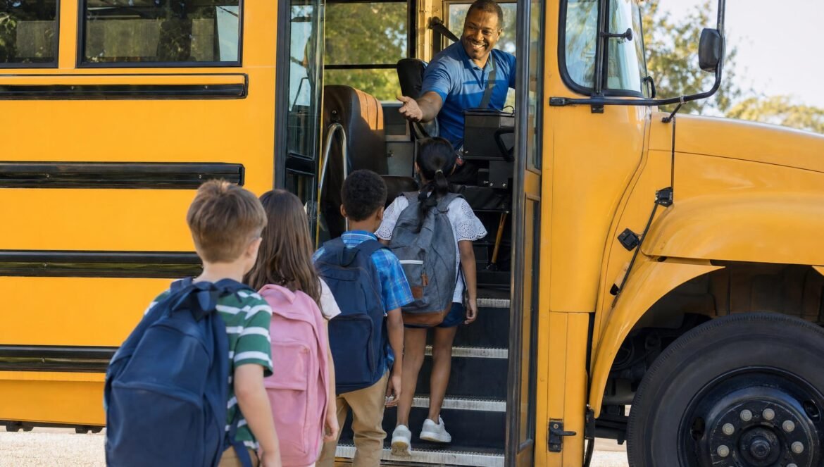 Young students with backpacks boarding a yellow school bus while the smiling adult driver greets them at the open door bright morning light
