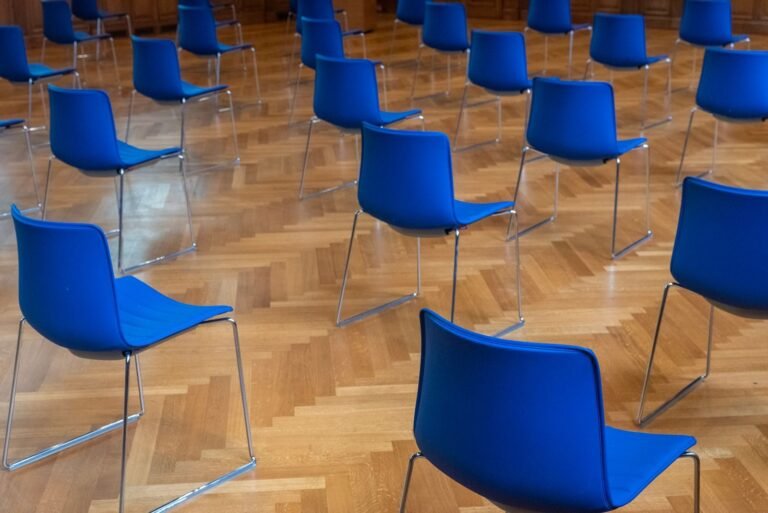 Empty room with blue chairs on a wooden parquet floor, arranged in rows