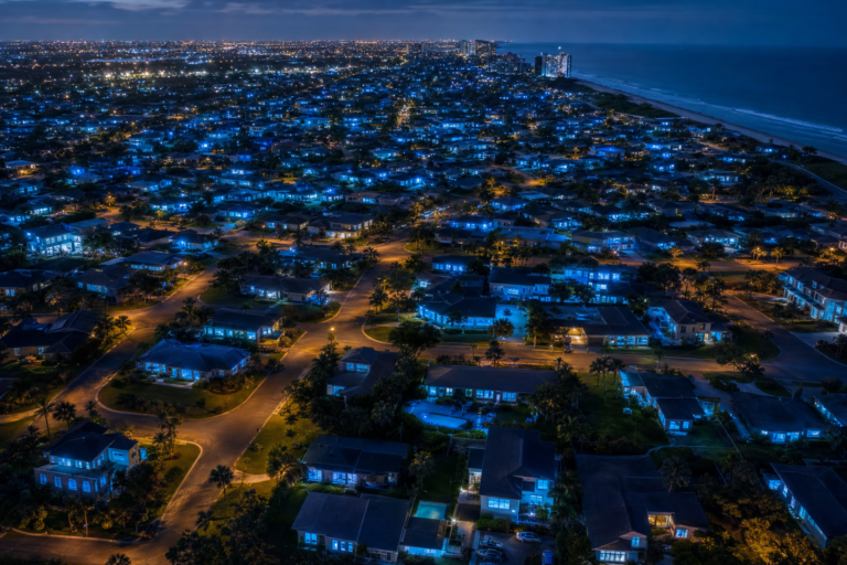 Night aerial of homes glowing with laptop light, the growth of online learning