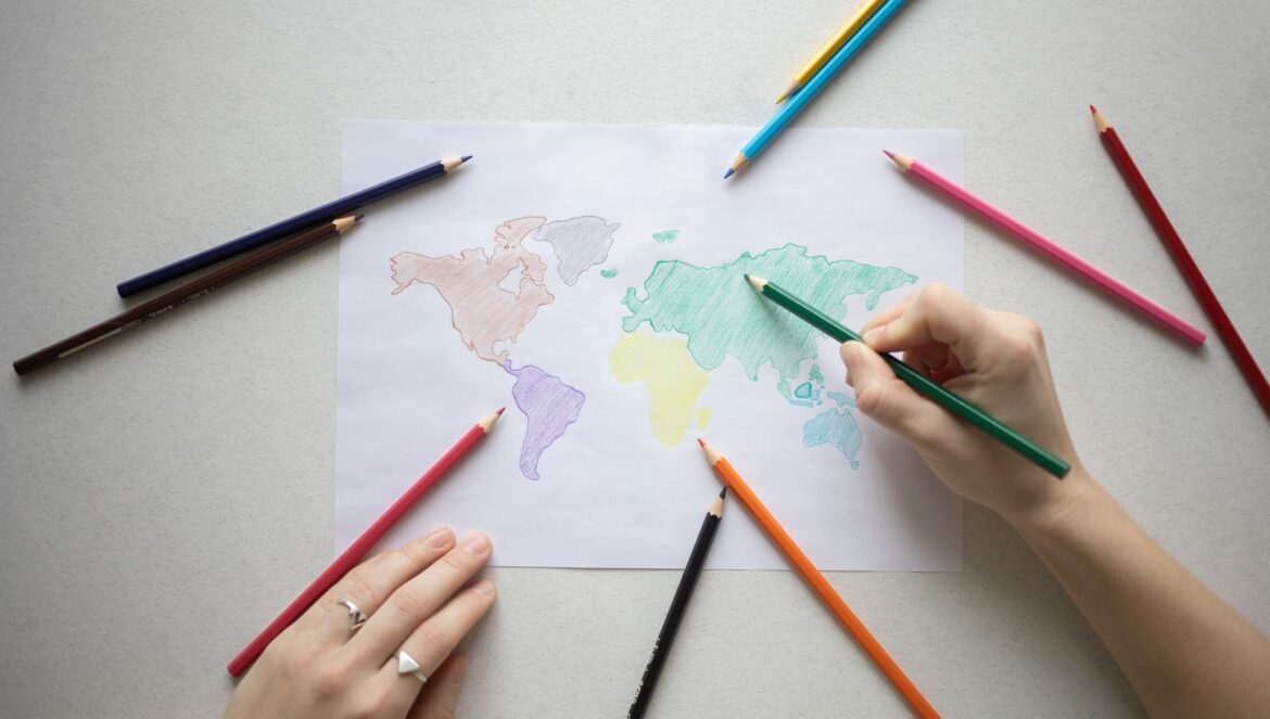 Hands coloring a world map on paper with colorful pencils creative learning