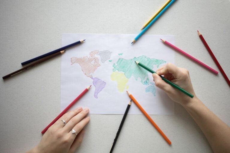 Hands coloring a world map on paper with colorful pencils, creative learning