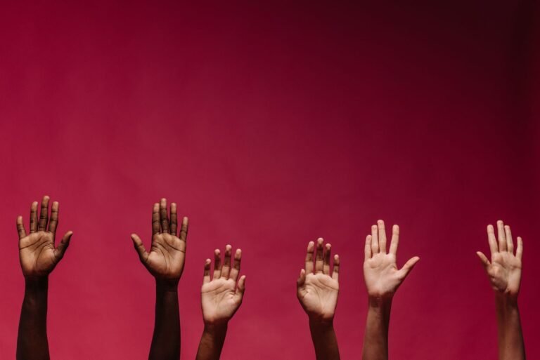 Image of diverse raised hands against a vibrant red background, symbol