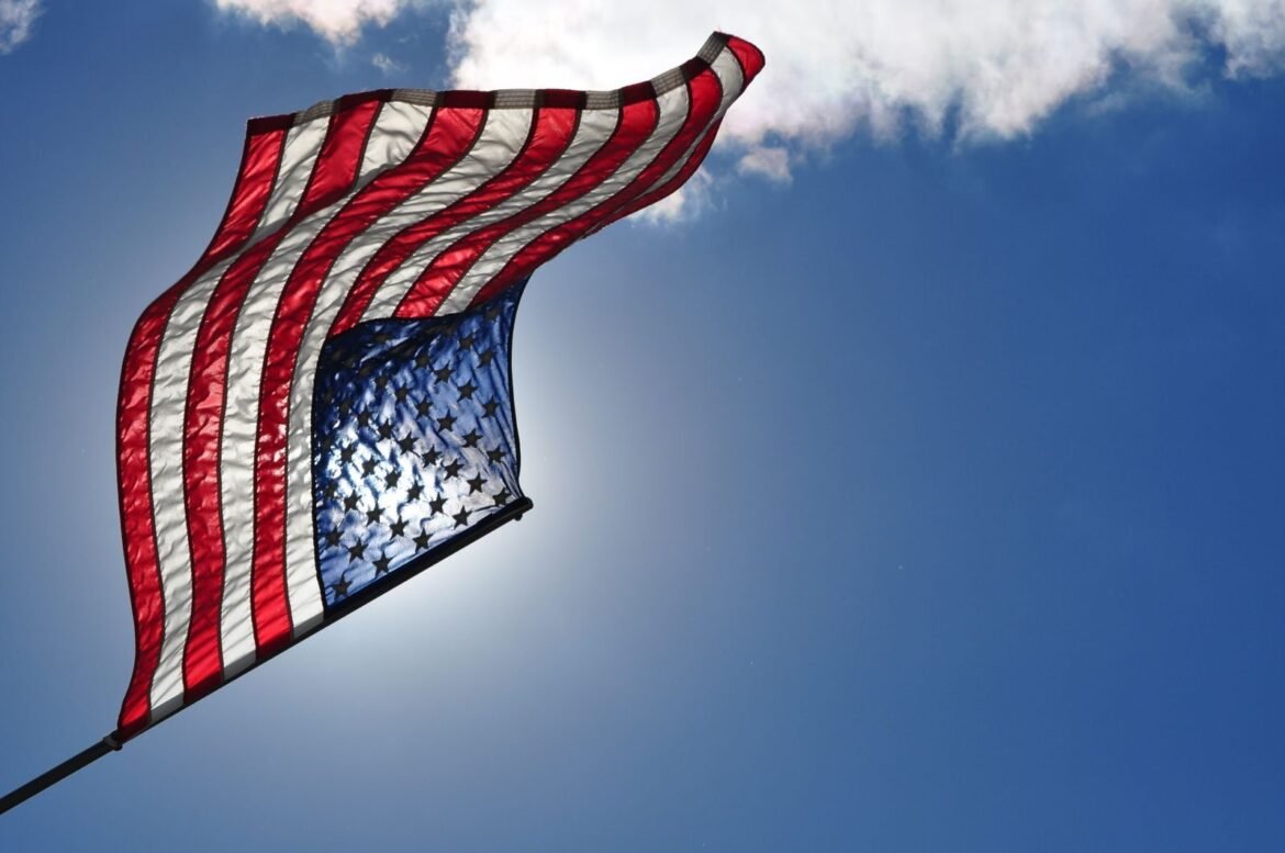 Low-angle view of the American flag waving against a bright blue sky on a sunny day