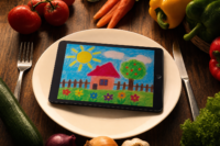 Tablet on a dinner plate showing a childs digital painting beside vegetables screen time that is not junk food