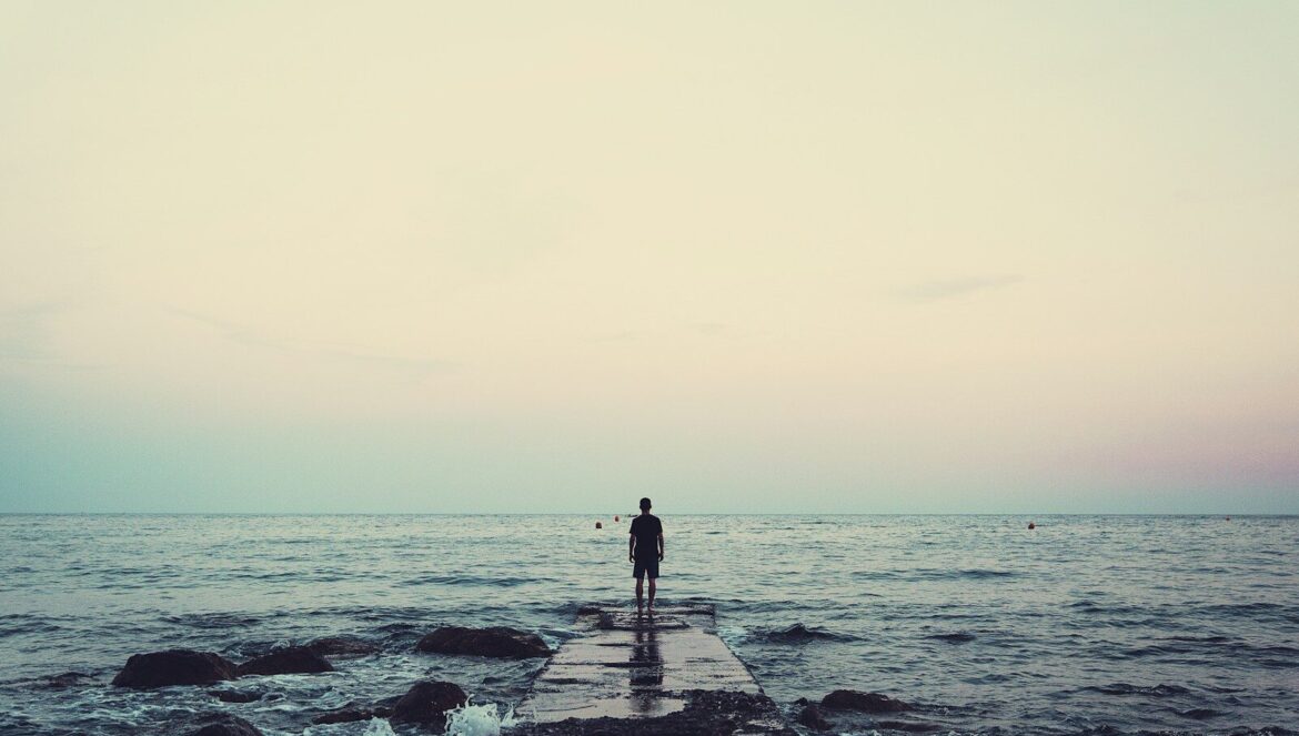 Silhouette of person standing on sea dock under cloudy sky