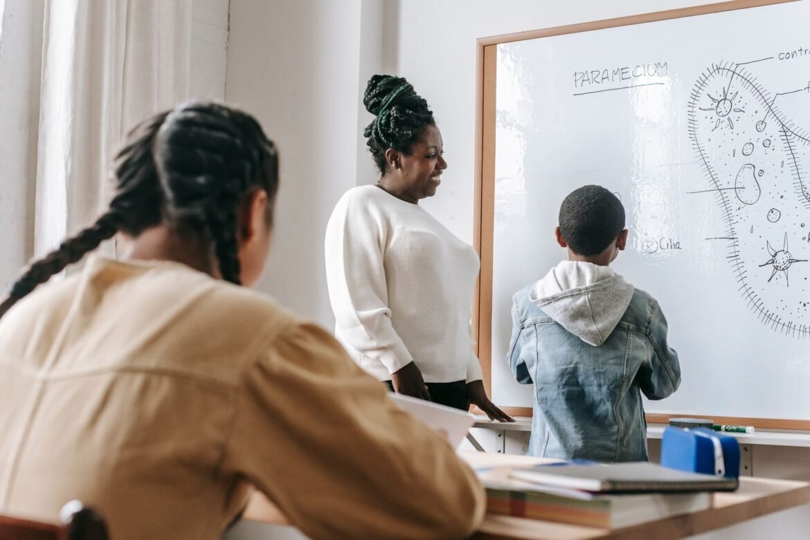 Smiling female teacher near a whiteboard with an illustration and diverse schoolchildren