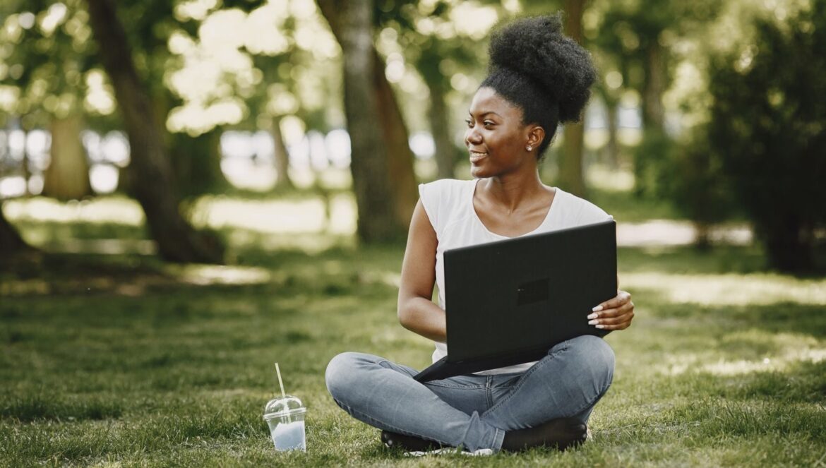 Smiling woman with laptop sitting in a sunny park enjoying a relaxing | edCircuit Smiling woman with laptop sitting in a sunny park enjoying a relaxing