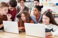 Teenage students actively collaborate on laptops in an educational environment with guidance from a teacher