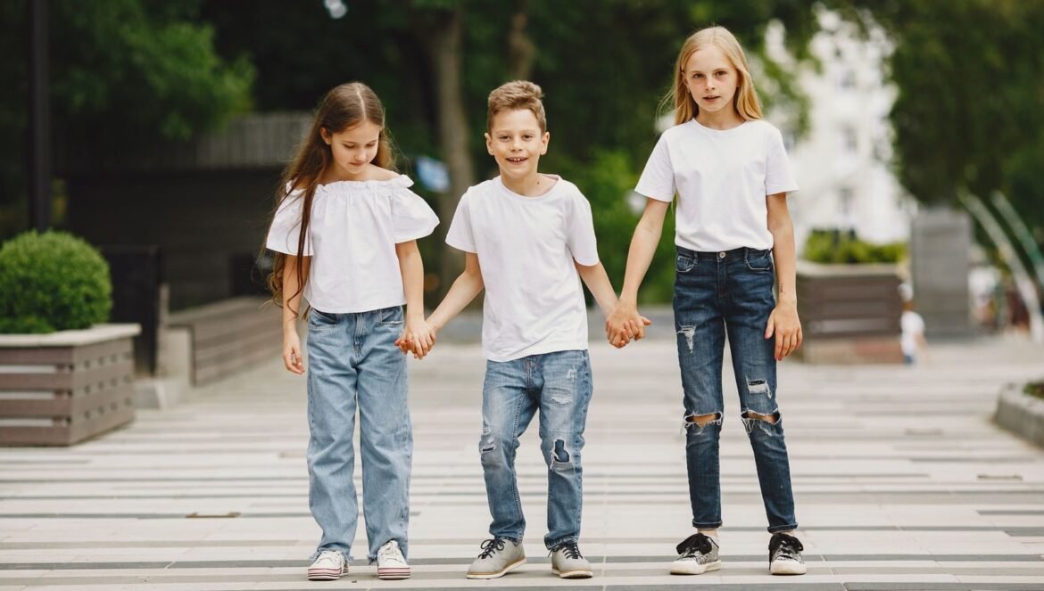 Three children in white tshirts and jeans holding hands outdoors on a | edCircuit Three children in white t shirts and jeans holding hands outdoors on a