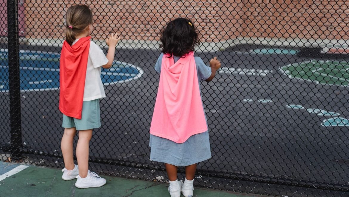 Two children wearing capes look through a playground fence embracing imagination | edCircuit Two children wearing capes look through a playground fence embracing imagination