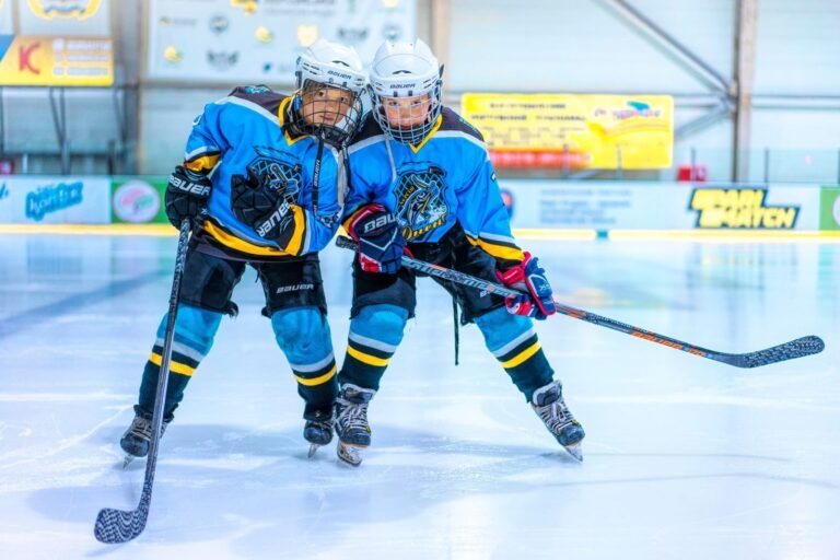 Two female ice hockey players in blue jerseys on a rink, engaged in a game