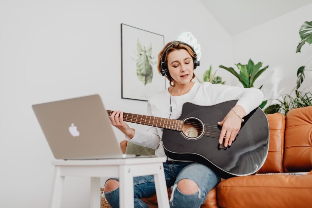 Woman playing guitar with headphones in a cozy living room using lapt | edCircuit Woman playing guitar with headphones in a cozy living room using lapt
