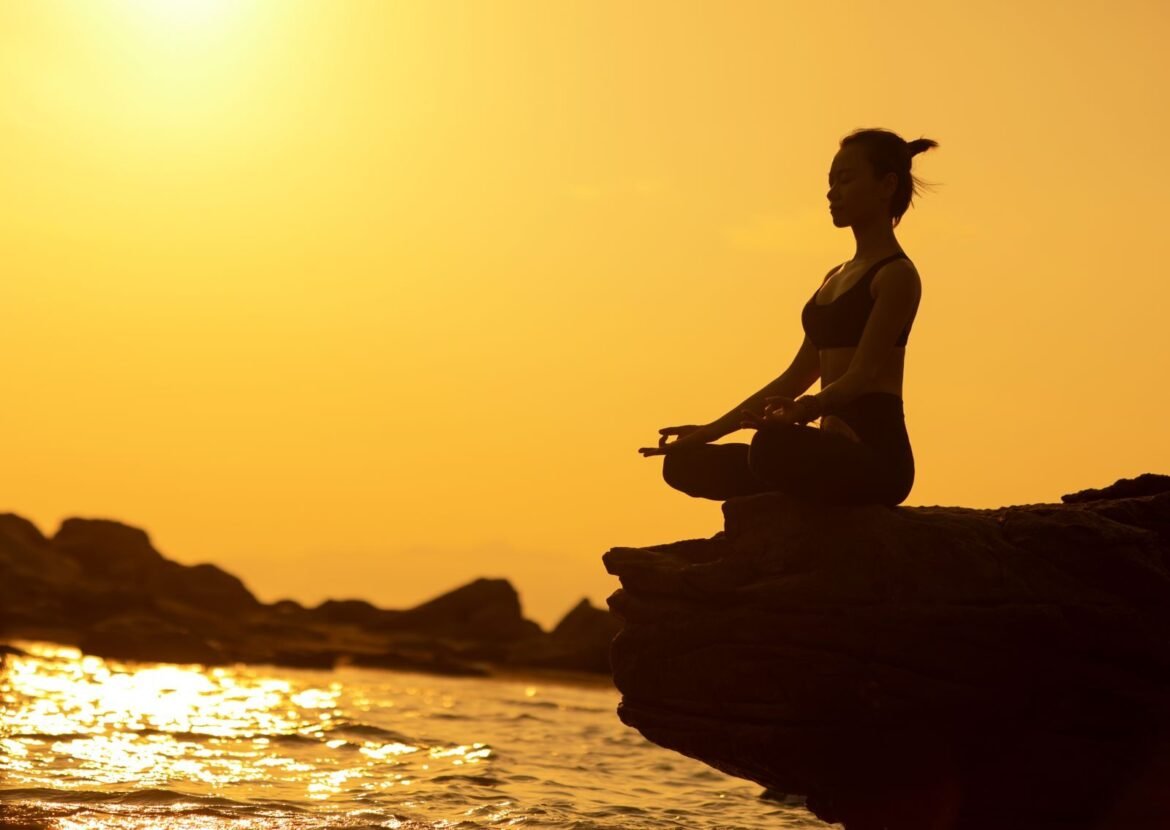 Woman practicing yoga in lotus pose on a cliff by the sea at sunset, embodying tranquility and balance