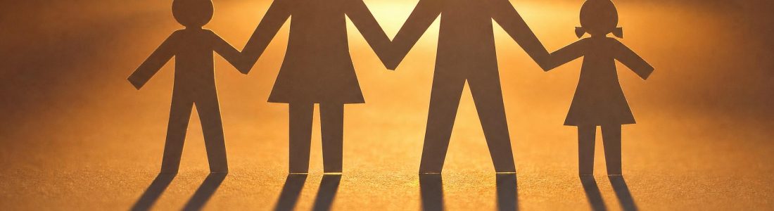A row of paper cut-out family figures holding hands, backlit by warm orange light casting long shadows