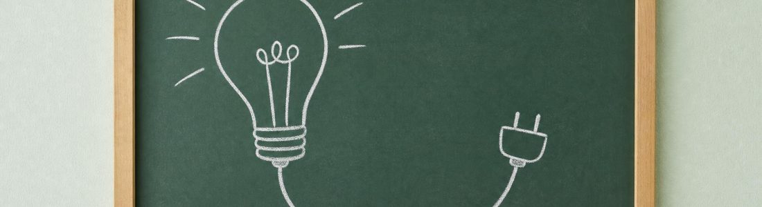 A framed green chalkboard on a pale mint wall with a simple chalk drawing of a light bulb whose cord ends in a plug, soft even light